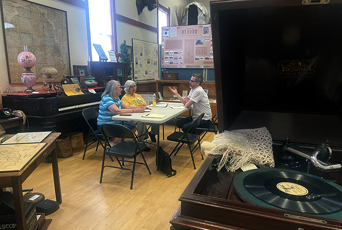 Three people at table talking. Victrola in foreground of photo